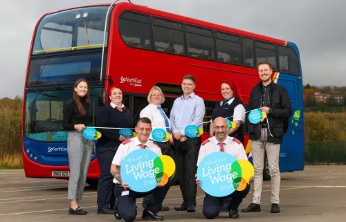 Go ahead bus group celebrate Living Wage accreditation with group of workers posing in front of a red double decker bus with a Living Wage Employer logo and bunting