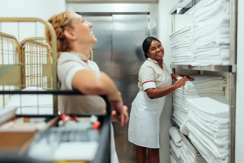 Two hotel maids laugh and joke in a linen cupboard.