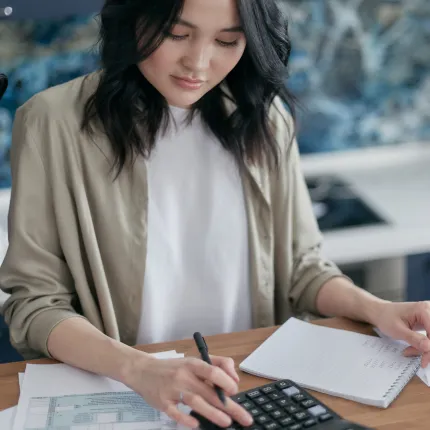 Young woman in an office using a calculator and taking notes