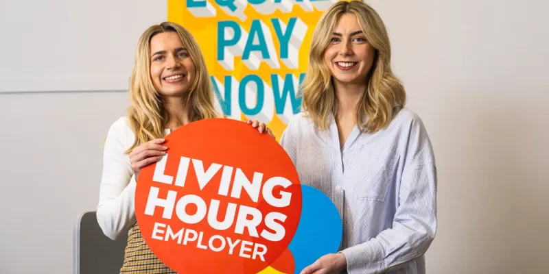Two women with Living Hours Employer sign