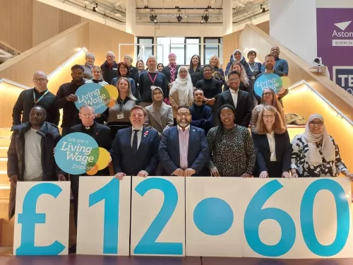 Group picture of people posing at a Living Wage Week event hosted by West Midlands Combined Authority holding up a sign with the Living Wage rate of £12.60